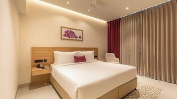A hotel room with a large bed, a bedside table with a phone, a chair, and a window with curtains.