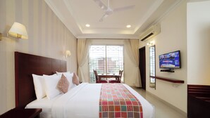 A hotel room with a large bed, a TV on the wall, a ceiling fan, and a window with curtains. - Lilac by Tamara 3rd Block Jayanagar (Bengaluru)