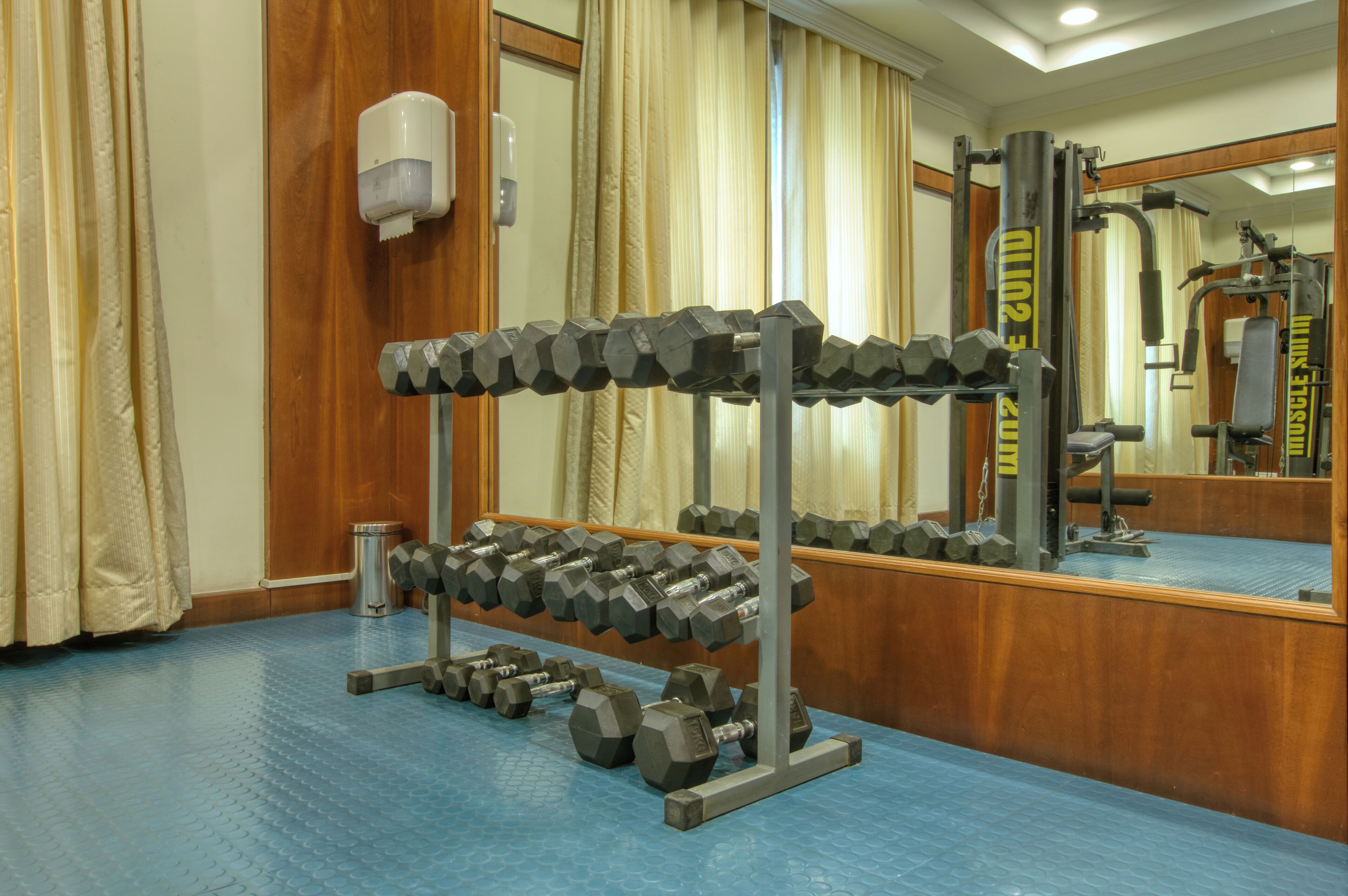Ein Fitnessraum mit Spiegelwand, Hantelgestell und blauem Boden.