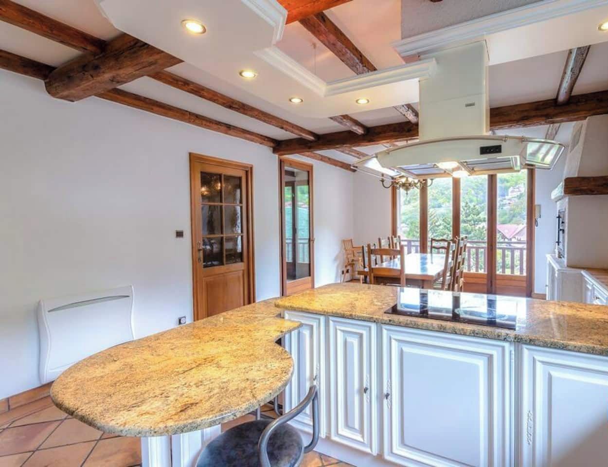 A kitchen with a large island, white cabinetry, and exposed wooden beams.