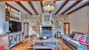 A cozy living room with exposed wooden beams, a stone wall, a fireplace, a TV, and a sofa.