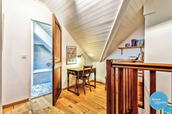 A room with a wooden floor, a desk with a chair, a bookshelf, and a sloped ceiling.