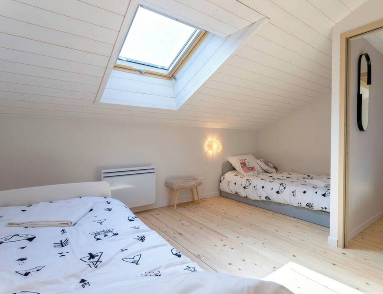 A bedroom with a sloped ceiling, a skylight, a bed with patterned bedding, a bedside table, and a wall-mounted light fixture.