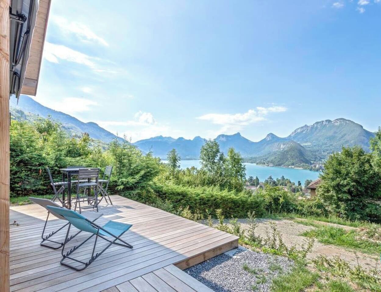 A wooden deck with outdoor furniture, overlooking a mountainous landscape and a lake.