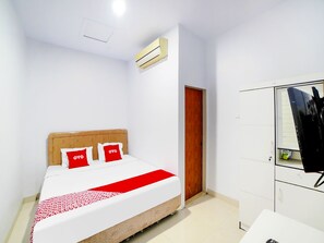 A hotel room with a bed, a wardrobe, a door, and an air conditioning unit.