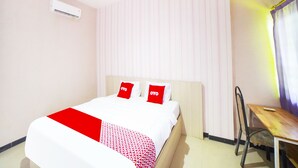 A hotel room with a bed, a desk, and an air conditioning unit.