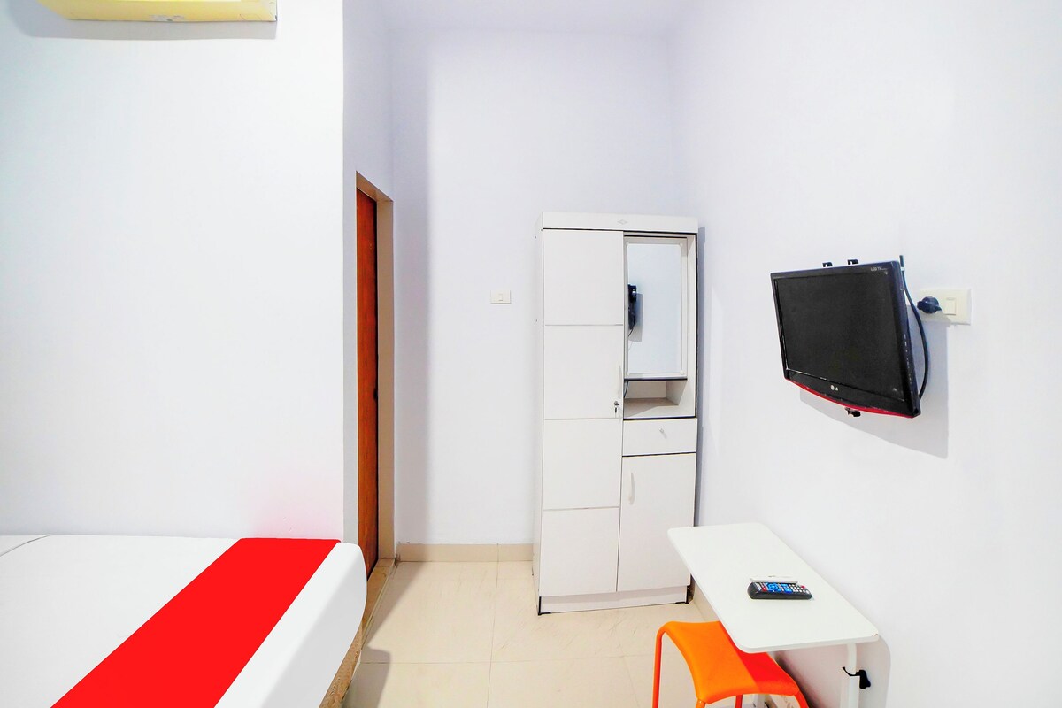 Una habitación pequeña y limpia con cama, escritorio, silla, televisor y armario.