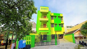 A multi-story building with a green and yellow facade, a gated entrance, and a visible motorcycle parked outside.