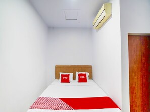 A small, narrow room with a single bed, two pillows with 'OYO' branding, a white ceiling, and a wooden door.