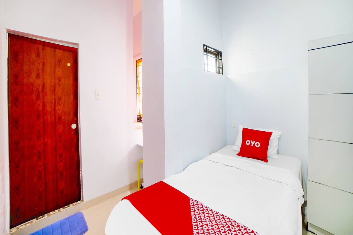 Ein Hotelzimmer mit roter Tür, einem weißen Bett mit rotem Kopfkissen und einem weißen Schrank.