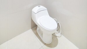 A small, white toilet in a corner of a bathroom with plain white tiles.