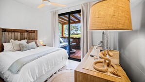 A bedroom with a bed, a wooden headboard, a ceiling fan, a large woven lamp, and a view of an outdoor deck.