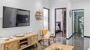 A modern living room with a large flat-screen TV, wooden furniture, and a glass door leading to a bedroom.