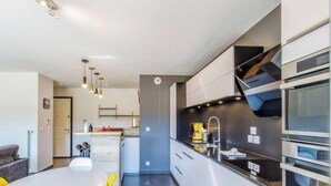 A modern kitchen with a central island, stainless steel appliances, and a dining area with a white table and yellow chairs. - T4 Terre EO - close to Lake Annecy. (Menthon-Saint-Bernard)