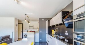 A modern kitchen with built-in appliances, a dining area with a table and chairs, and a visible door leading to another room.