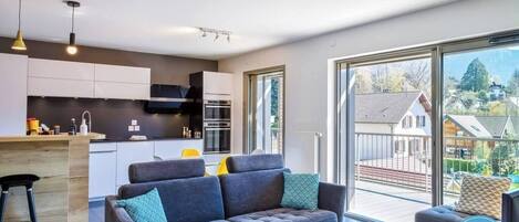 Un apartamento moderno con cocina, sofá y balcón con vista a casas.