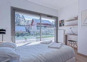 A bedroom with a large sliding glass door, a bed, a small table, and a chair.