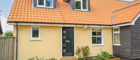 A two-story house with a tiled roof, a front door, and a small garden area.