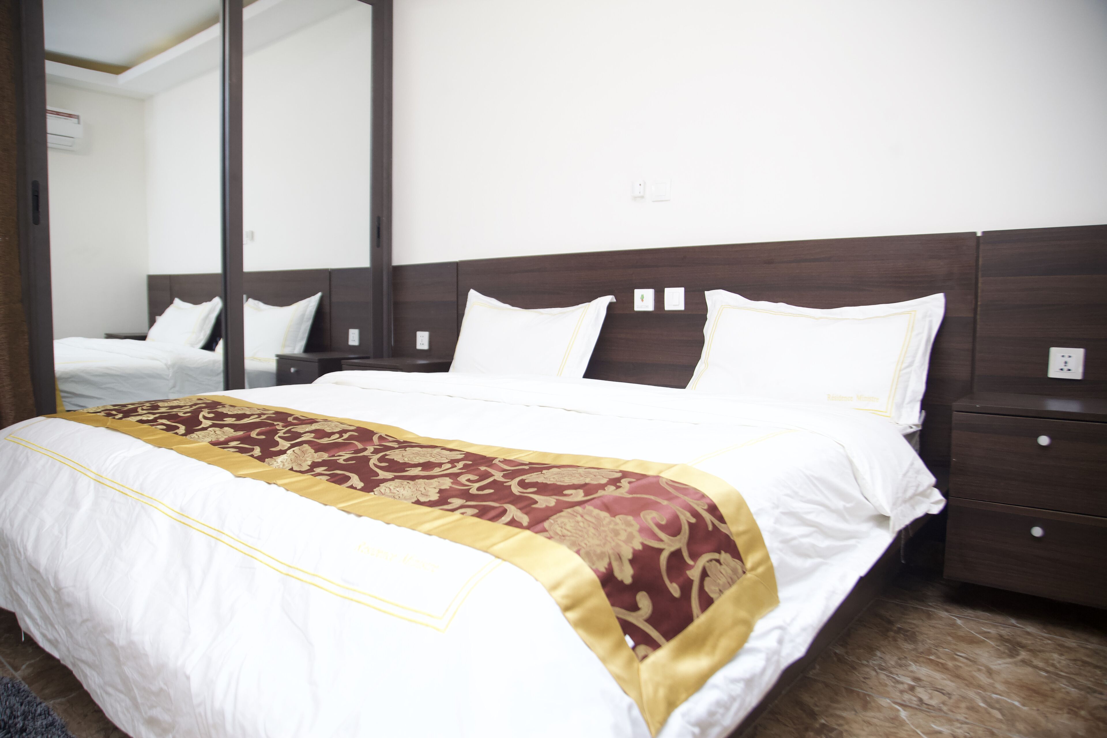 A hotel room with a large bed, a wooden headboard, a nightstand, and a mirror.