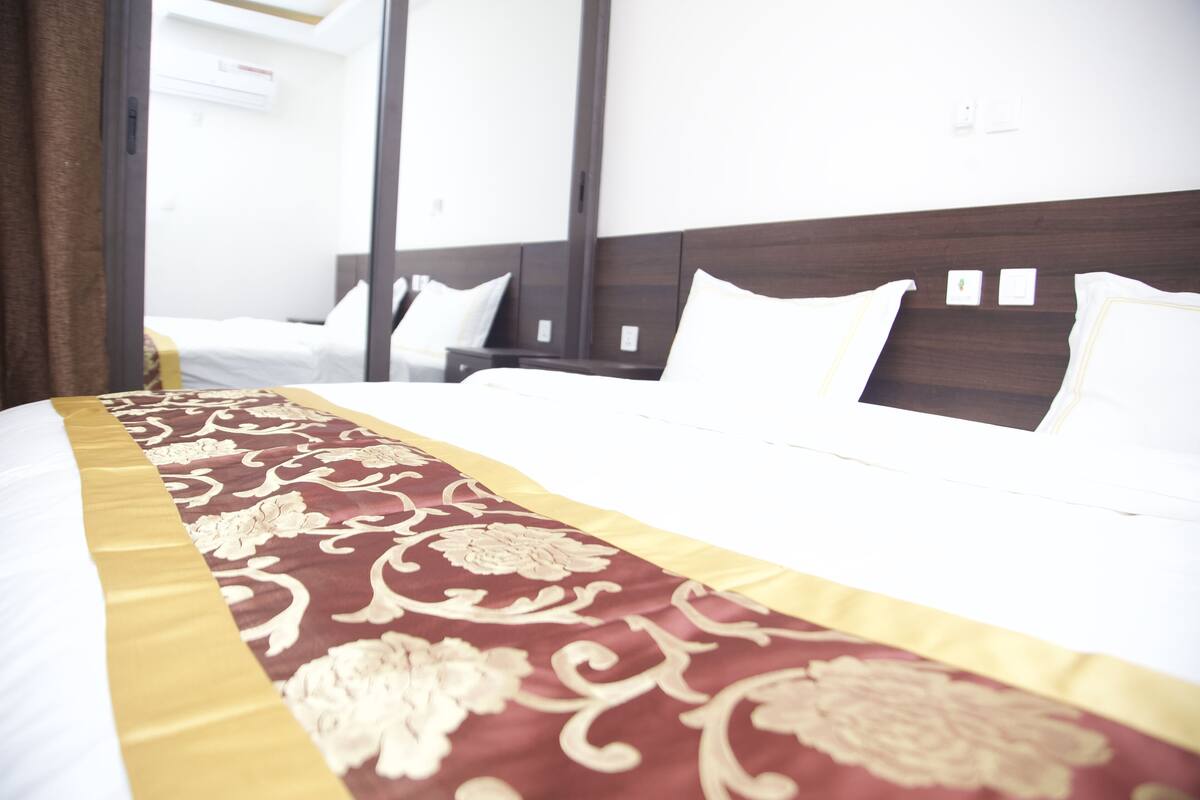 A hotel room with a large bed, a wooden headboard, and a decorative bed runner.
