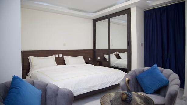 A hotel room with a large bed, two armchairs, a small coffee table, and a large mirror. - Residence Ministre (Abidjan)