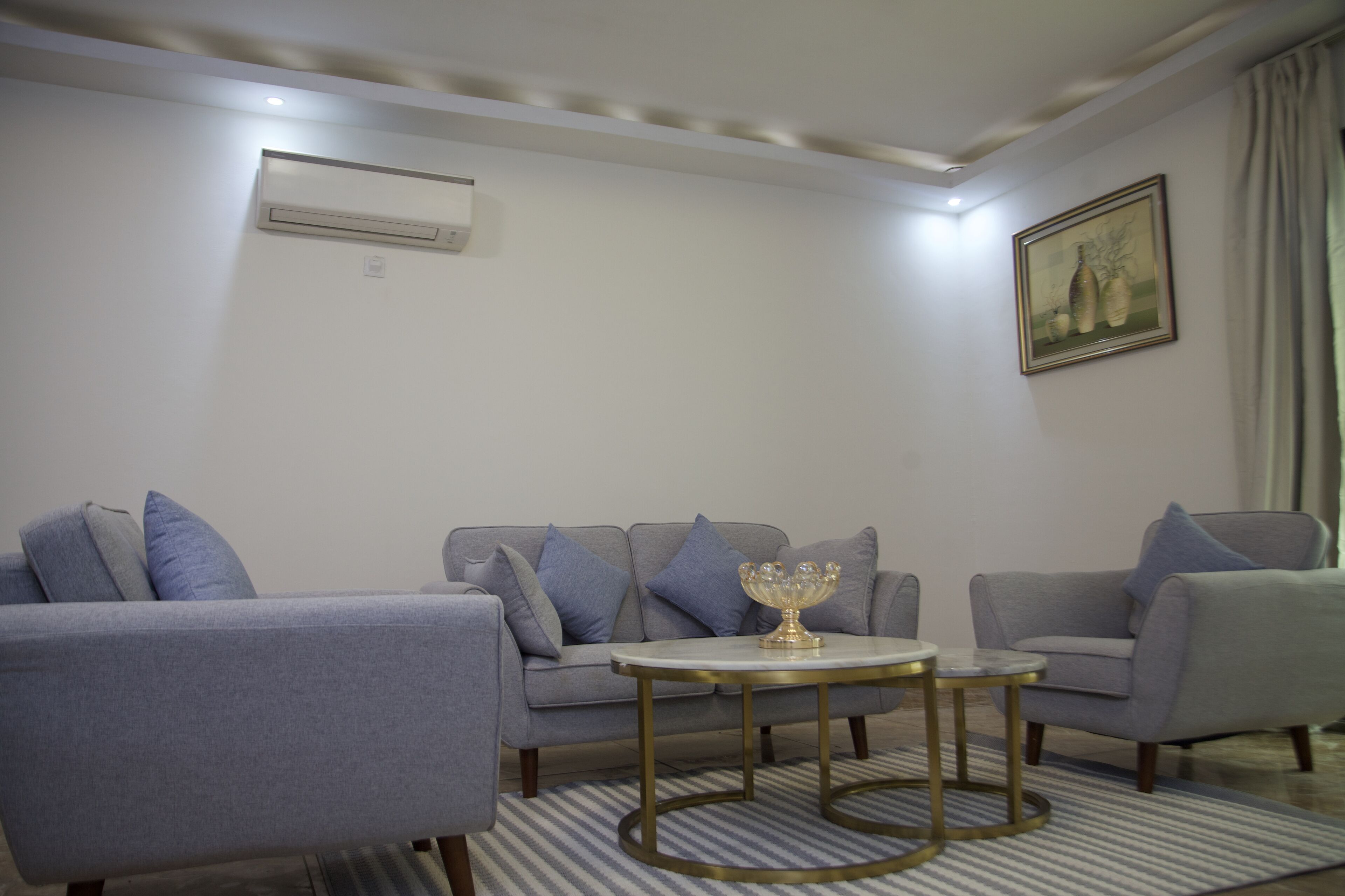 A modern living room with a grey sofa set, a round coffee table, and a painting on the wall.