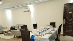 A dining area with a long table set for a meal, a sofa, and a door in the background. - Residence Ministre (Abidjan)