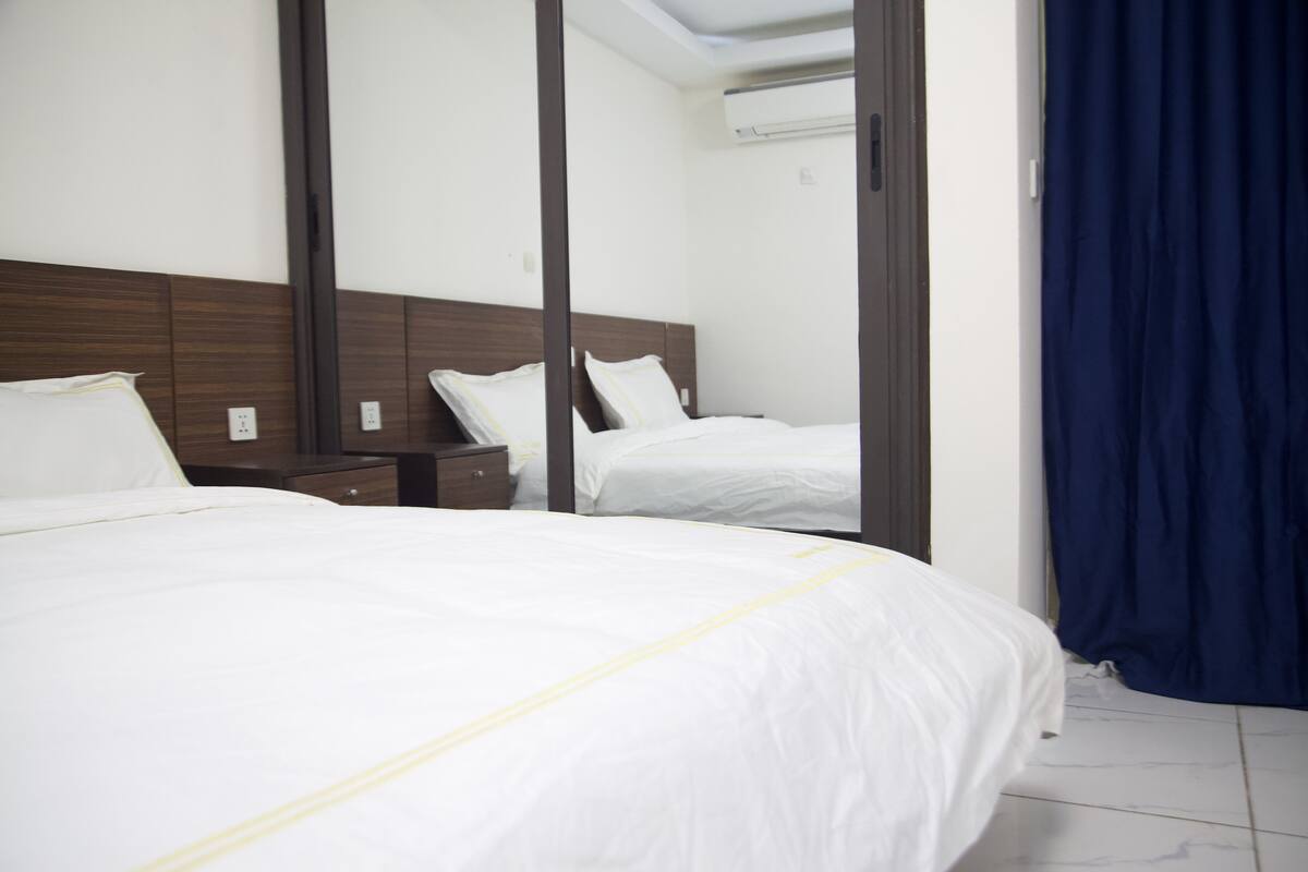A hotel room with a large bed, a nightstand, a mirror, and a blue curtain.