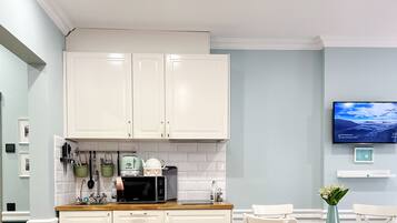 A modern kitchen with white cabinets, a microwave, and a coffee maker. There is a TV mounted on the wall displaying a scenic view.