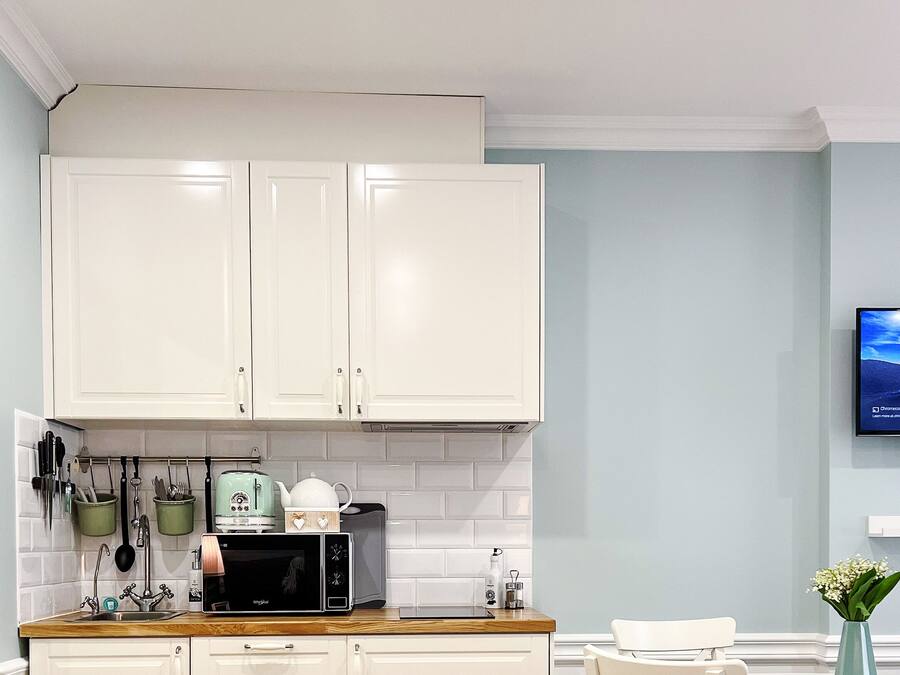 Una cocina moderna con armarios blancos, un microondas y una cafetera. Hay un televisor en la pared que muestra una vista panorámica.