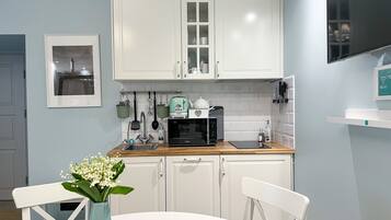 A modern kitchen with white cabinets, a microwave, and a sink. There is a vase with flowers on the table.