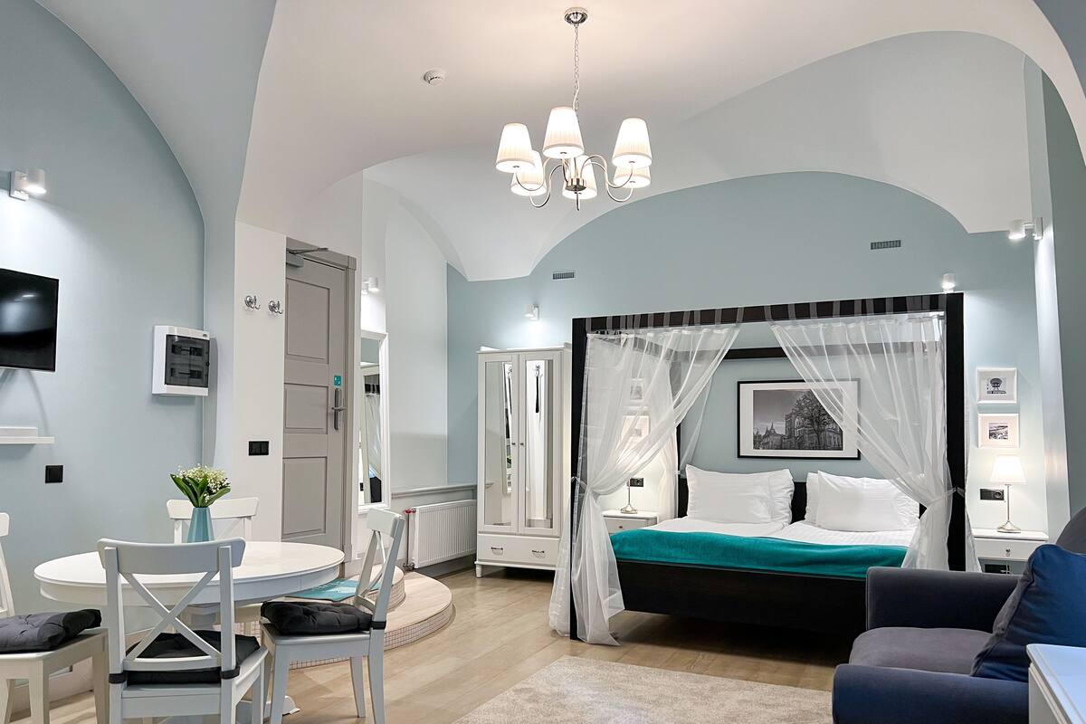 A bedroom with a four-poster bed, a round dining table, and a TV mounted on the wall.