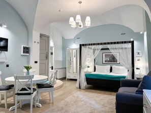 A bedroom with a four-poster bed, a round dining table, and a TV mounted on the wall. - Revelton Suites Riga (Riga)