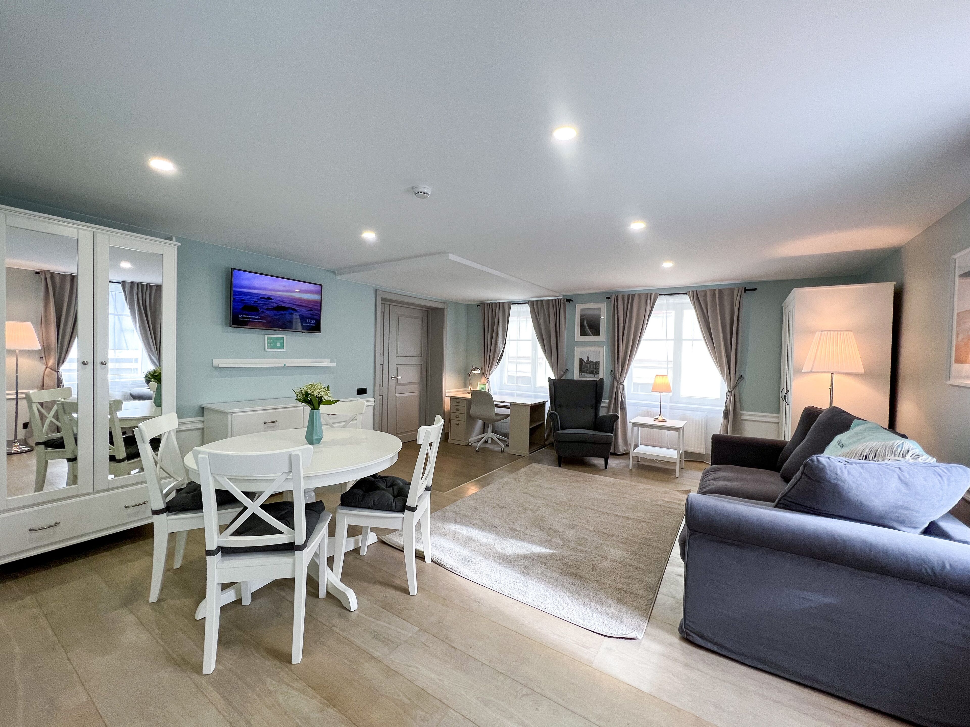 A spacious living area with a dining table, chairs, a sofa, and a TV mounted on the wall.