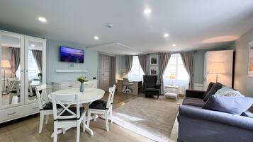 A spacious living area with a dining table, chairs, a sofa, and a TV mounted on the wall.