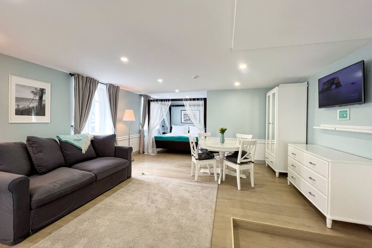 A modern hotel room with a bed, a dining table, a sofa, and a TV.