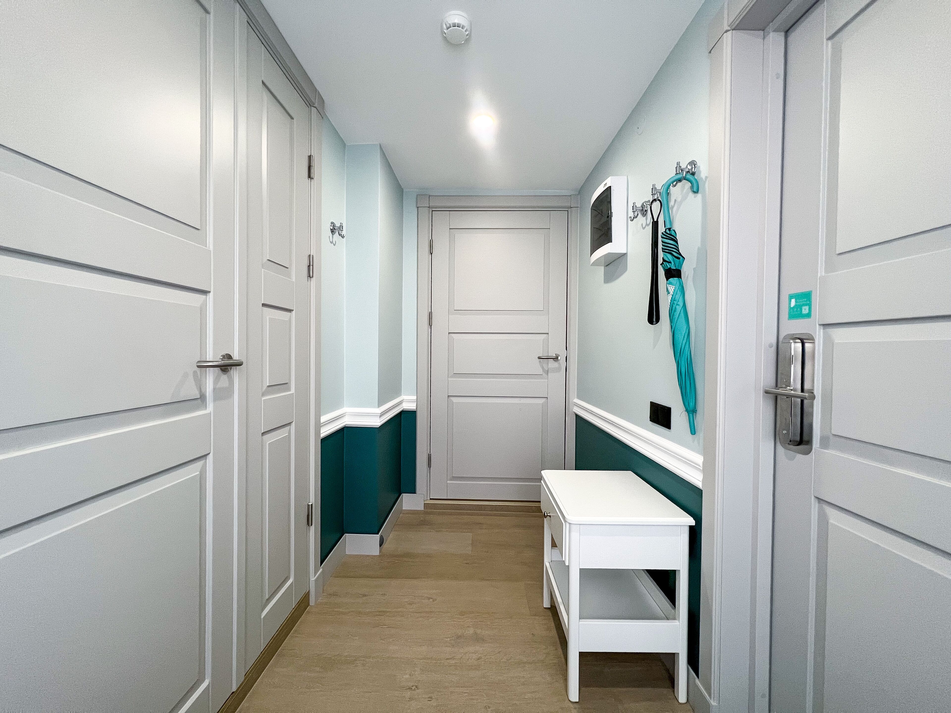 A narrow hallway with white doors, teal walls, a white bench, and a towel rack.