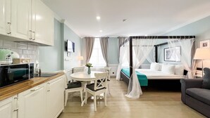 Habitación de hotel compacta con kitchenette, comedor, cama con dosel y sofá.