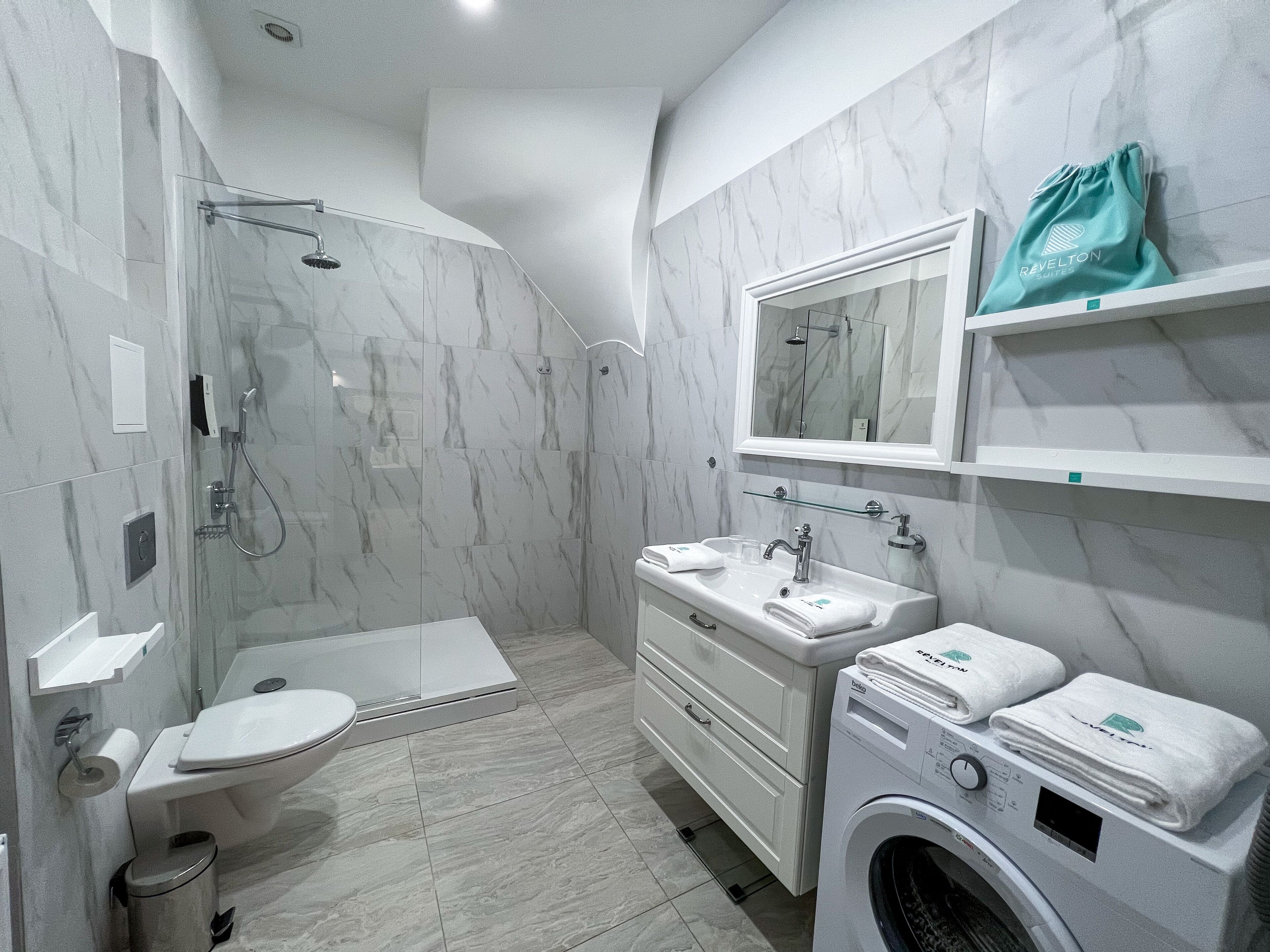 A modern bathroom with a glass-enclosed shower, a sink with a mirror above, and a washing machine.