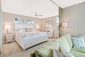 Ein Schlafzimmer mit einem Bett, Nachttischen, einer Kommode, einem grünen Sofa und Kunstwerken an den Wänden.