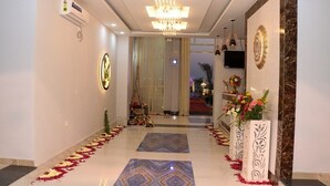 Un hall d’hôtel avec un lustre, un comptoir d’accueil et un tapis rouge menant à une salle.