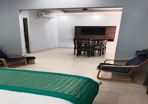 A hotel room with a bed, a dining table with chairs, a TV mounted on the wall, and a seating area with chairs. - M Resort (Sikandarabad)