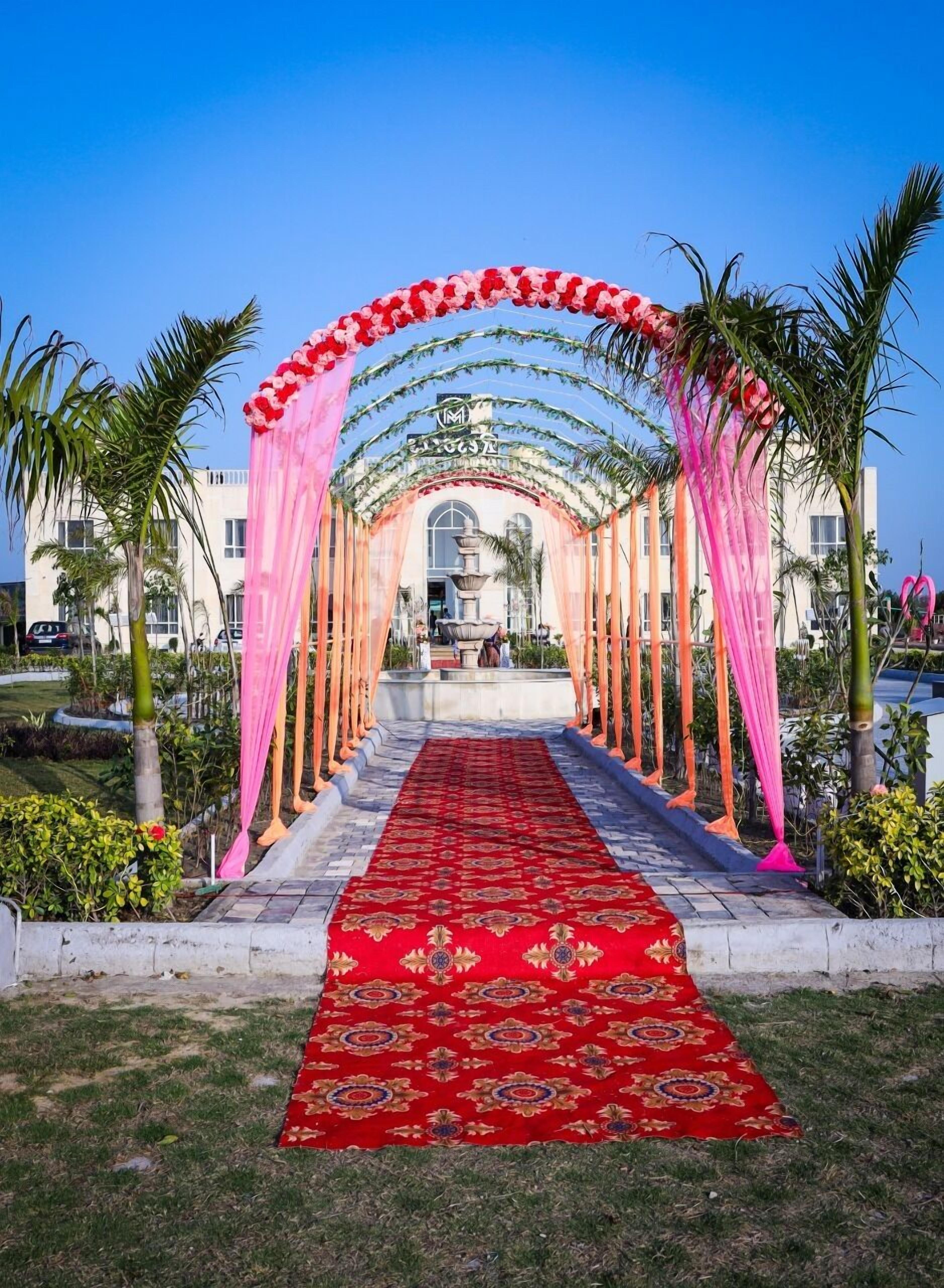 Um tapete vermelho que leva à entrada de um edifício com um arco rosa e palmeiras.