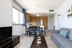 A modern living room with a flat-screen TV, a grey sofa with blue cushions, a wooden dining table with chairs, and a kitchen in the background. - Beachfront apartment with sea views - UHC PANORAMIC (Miami Playa)