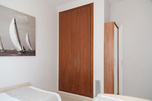 A bedroom with a wooden wardrobe, a bed with a white headboard, and a painting of sailboats on the wall.