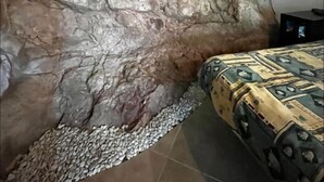 A room with a stone wall, a green light strip, a bed with patterned bedding, and a tiled floor. - Refugi per Boletaires i Amants de la Natura (La Nou de Berguedà)