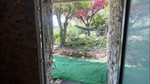 A window with a view of a garden, including a hammock and a green mat. - Refugi per Boletaires i Amants de la Natura (La Nou de Berguedà)