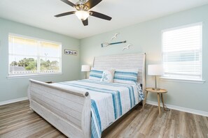A bedroom with a bed, two bedside tables, a ceiling fan, and a window with blinds.
