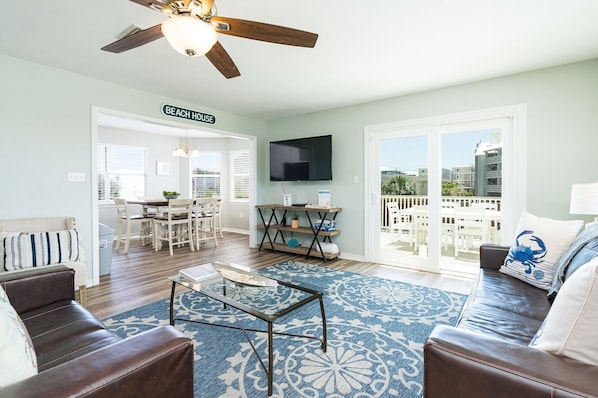 A spacious living room with a dining area, a ceiling fan, a TV, and a balcony with a view.