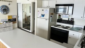 A modern kitchen with white cabinets, a stainless steel microwave, a stove, and a refrigerator. There is a chalkboard menu on the wall and a door with a glass panel leading to another room. - Thunder Island 157D-Baywater 39th St, Internet, Pool, Elev, W/D, AC (Ocean City)